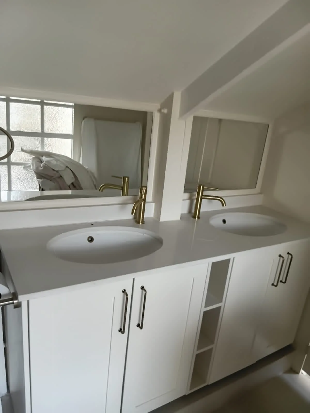 Double Vanity in White Shaker — A double bathroom vanity with two basins on a white top, brass mixers, shaker doors and an open shelf unit between them for towels.